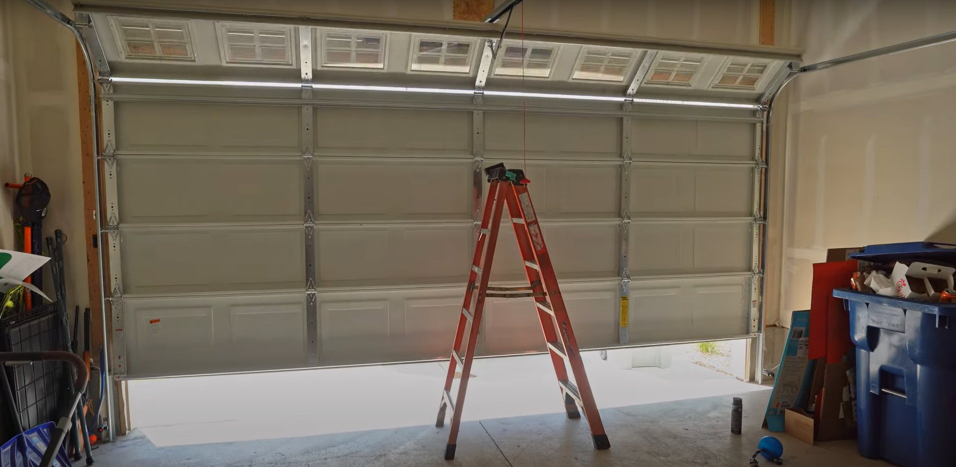 A professional technician installing a new, modern gray garage door on a residential home.