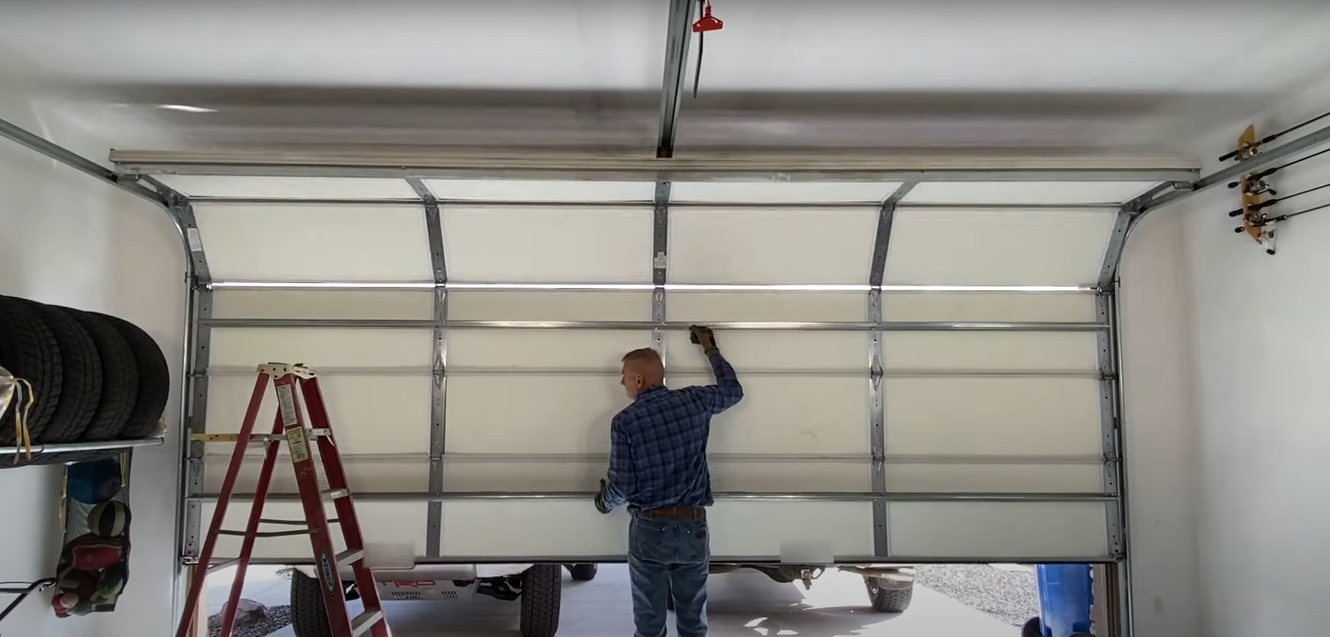 A technician performing overhead garage door repair on a residential silver door.