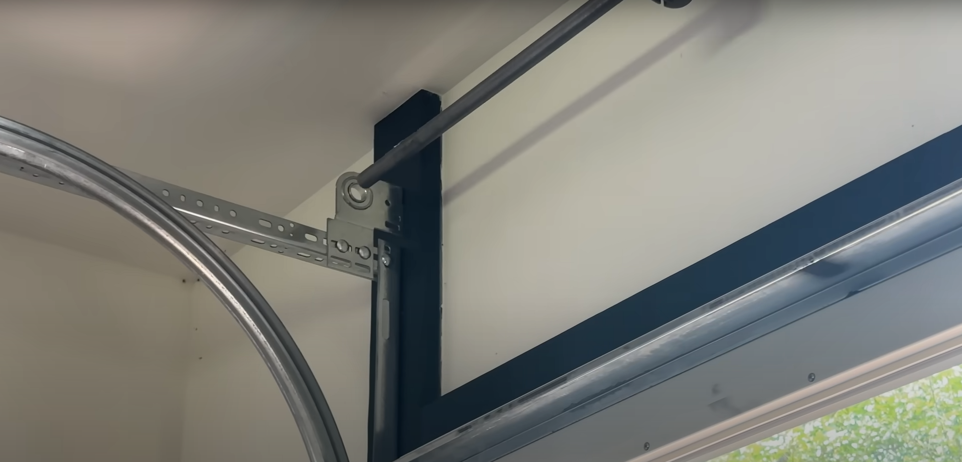 A close-up of a galvanized steel garage door track installed vertically against a garage wall.