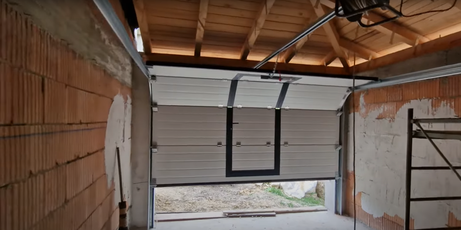 A technician performing overhead garage door repair on a residential silver door.