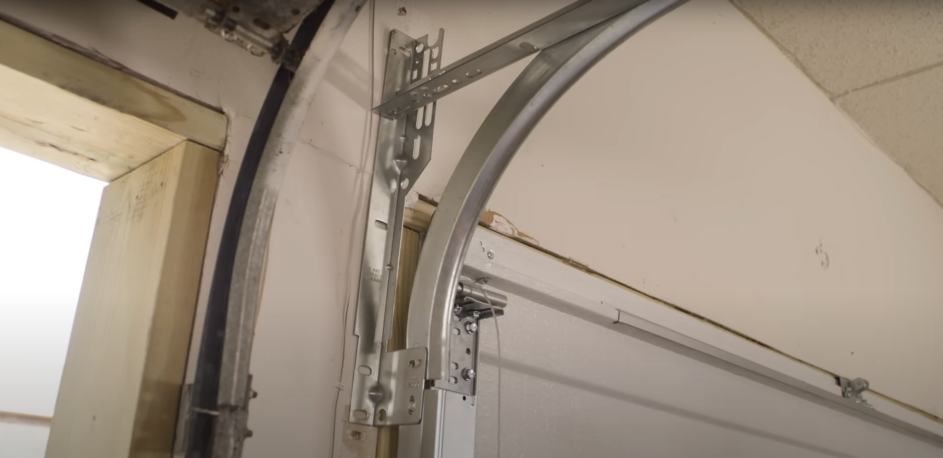 A close-up of a galvanized steel garage door track installed vertically against a garage wall.