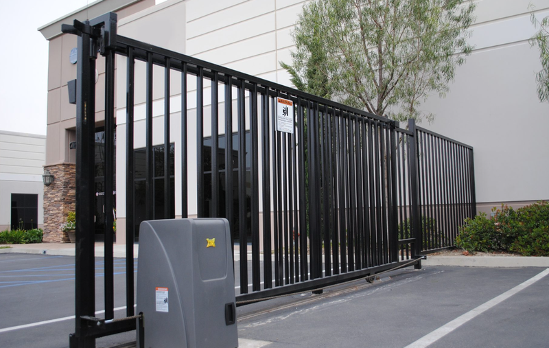 A technician kneels down to inspect and repair the mechanism of a modern automated driveway gate.